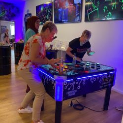 Mehrere Personen genießen das interaktive Tischspiel "Neuron Race" in einem lebhaft beleuchteten Raum voller Energie und Spaß.