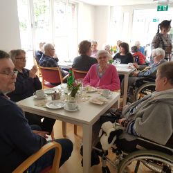 Mehrere ältere Menschen genießen Kaffee und Kuchen in einem hellen Raum, während sie sich lebhaft unterhalten.