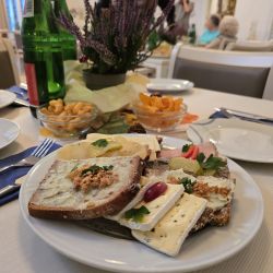 Ein Teller mit belegten Broten und Käse steht auf einem gedeckten Tisch, umgeben von Mineralwasser und Snacks.