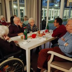 Ältere Menschen unterhalten sich lebhaft bei Getränken und Snacks an einem Tisch in einem gemütlichen Gemeinschaftsraum.