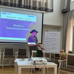 Ein Referent präsentiert Informationen zu sexualisierter Gewalt in einem Seminarraum mit Projektor und Flipchart.