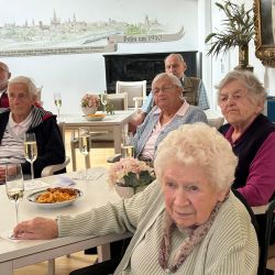 Ältere Menschen genießen ein Treffen mit Sekt und Snacks in einem hellen Raum mit einer Wandmalerei. | © Name