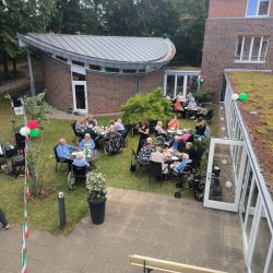 Menschen genießen ein geselliges Treffen im Freien neben einem modernen Backsteingebäude bei sonnigem Wetter.