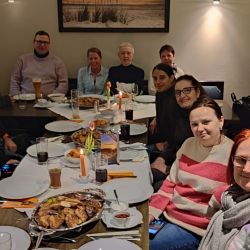 Zwölf Personen sitzen fröhlich in einem Restaurant um einen Tisch und genießen ein abwechslungsreiches Essen gemeinsam.