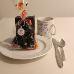 Ein weihnachtlich verpacktes Geschenk steht auf einem Teller neben einer Tasse und Besteck auf einem weißen Tisch.