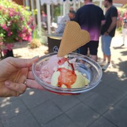 Eine Hand hält eine Schüssel mit Eis, garniert mit einem Herz-Waffelstück und Erdbeersauce.