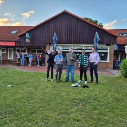 Fünf Männer posieren lächelnd vor einem Restaurant, während Gäste im Hintergrund entspannt miteinander sprechen. | © Name