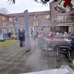 Menschen genießen eine festliche, winterliche Atmosphäre im Garten, während sie an Tischen im Freien beisammen sitzen.