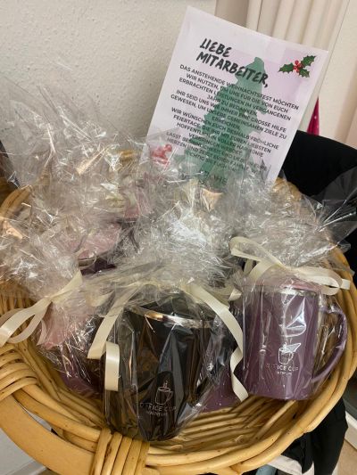 Ein Korb voller weihnachtlich verpackter Tassen und eine Dankeskarte für Mitarbeitende steht auf einem Tisch.