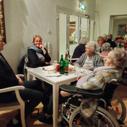 Ältere Damen sitzen lächelnd an einem Tisch in einem gemütlichen Raum und genießen ein geselliges Beisammensein.