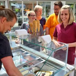 Eine Frau serviert Eiscreme an eine fröhliche Gruppe, die an einem Eiswagen mit verschiedenen Waffeln wartet.