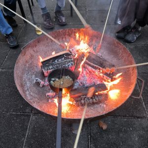 Personen rösten Marshmallows und Popcorn über einem offenen Lagerfeuer in einer Feuerschale und genießen die gemütliche Wärme.