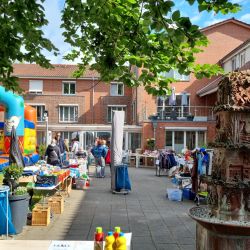 Ein bunter Flohmarkt mit Hüpfburg und Ständen belebt den sonnigen Innenhof eines charmanten Backsteinhauses.