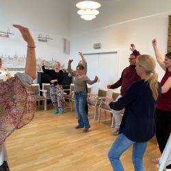 Eine Gruppe von Menschen tanzt fröhlich in einem Raum mit Holzboden und Wandgemälden.