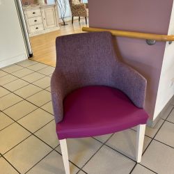 Ein violetter Stuhl steht auf gefliesten Boden in einer hellen Ecke, neben einer cremefarbenen Kommode im Flur.