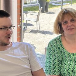 Ein Mann und eine Frau sitzen nebeneinander vor einem sonnigen Fenster und unterhalten sich angeregt.