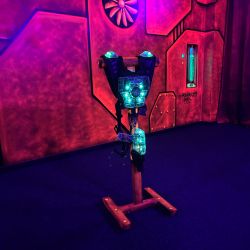 Ein leuchtendes Lasertag-Westen-Display erhellt einen neonfarbenen Raum mit futuristischer Wanddekoration.