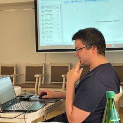 Ein Mann konzentriert sich auf seinen Laptop in einem Meetingraum, während eine Präsentation auf der Leinwand läuft.