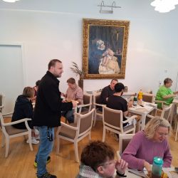 Menschen sitzen in einem gemütlichen Café und genießen ihre Mahlzeit, umgeben von Kunstwerken an der Wand.