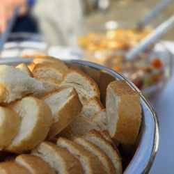 Frische Baguettescheiben liegen in einer Metallschüssel auf einem Tisch bei einem sonnigen Outdoor-Event.