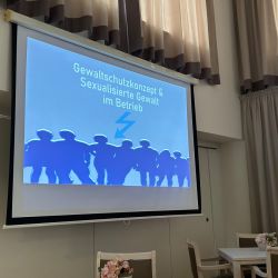 In einem Raum mit gedecktem Tisch wird eine Präsentation zu Gewaltprävention und Schutzkonzepten im Betrieb gezeigt.