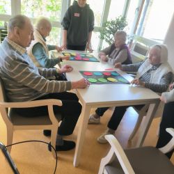Senioren und ein Betreuer spielen gemeinsam an einem Tisch mit bunten Kreisen und fördern so soziale Interaktion.