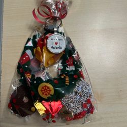 Ein weihnachtlich dekorierter Geschenkanhänger mit "El. mit Herz Melanie" liegt auf einem Tisch neben verpackten Keksen.