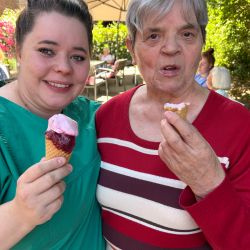 Zwei Frauen genießen Eis im sonnigen Garten, umgeben von bunten Blumen und fröhlicher Atmosphäre.
