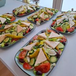 Fünf bunte Salatteller mit Tomaten, Gurken, Peperoni und Käsestücken auf einem Tisch.