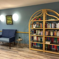 Ein moderner Lesebereich zeigt einen blauen Sessel, einen runden Tisch und ein gut gefülltes Bücherregal vor einer blauen Wand.