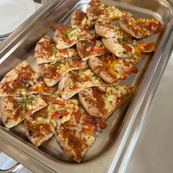 Frisch gebackene Pizzastücke mit Paprika und Käse liegen appetitlich in einer Edelstahlschale bereit.