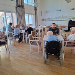 Eine Gruppe von Senioren und Betreuern spielt zusammen in einem hellen, freundlichen Gemeinschaftsraum.