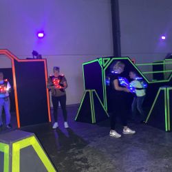 Personen spielen ein spannendes Lasertag-Spiel in einer Halle mit leuchtenden, neonfarbenen Hindernissen.