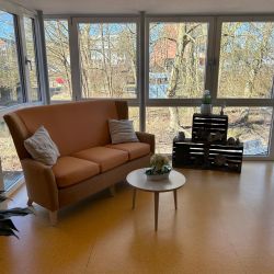 Ein sonniger Raum mit einem braunen Sofa, einem runden Tisch und Holzkisten strahlt eine gemütliche Atmosphäre aus.