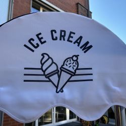 Ein Sonnenschirm mit stilisierten Eistüten und der Aufschrift "Ice Cream" steht vor einem Backstein-Gebäude.
