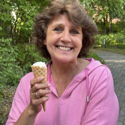 Eine lachende Frau im rosa Hoodie genießt an einem sonnigen Tag im Freien ein Eis.