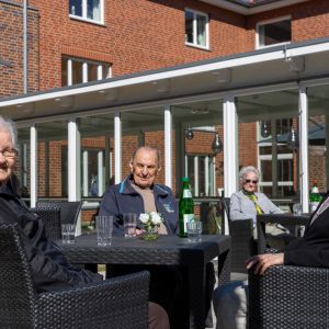 Vier Senioren genießen sonnige Stunden auf einer Terrasse, umgeben von Pflanzen und Getränken. | © Name