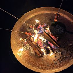 Würstchen werden über einem offenen Feuer auf Spießen gegrillt, während die Flammen lebhaft lodern.