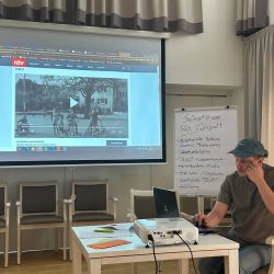 Ein Referent präsentiert ein Video über Schutz vor sexueller Gewalt in einem Seminarraum.