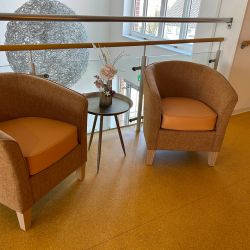 Zwei bequeme Sessel stehen neben einem Tisch mit Blumen auf einem modernen, gelben Boden in einem hellen Raum.