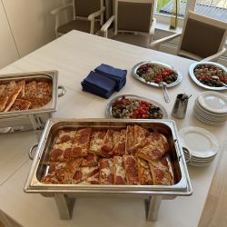 Tabletts mit Pizza und Tellern sind auf einem Tisch arrangiert, umgeben von Schalen mit Antipasti und Servietten für das Buffet.