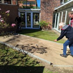 Zwei Personen spielen im Garten Boule, während eine Magnolie blüht und die Sonne scheint. | © Name