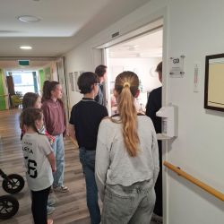 Eine Gruppe von Kindern und Erwachsenen wartet am Eingang eines Raums in einem flurartigen Bereich.