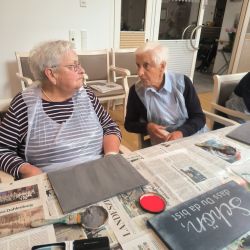 Zwei ältere Damen unterhalten sich während eines kreativen Malprojekts in einem Gemeinschaftsraum. | © Name