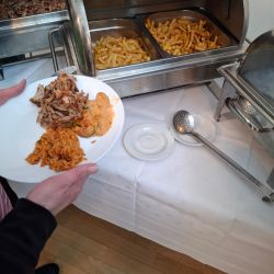 Eine Person serviert sich Pommes und Fleisch von einem Buffet auf einen Teller.