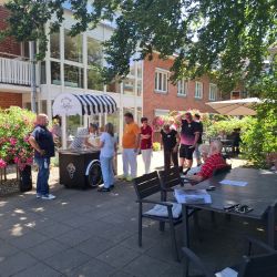 Eine Gruppe von Menschen genießt Eiscreme an einem sonnigen Tag im Garten eines Wohnheims. | © Name