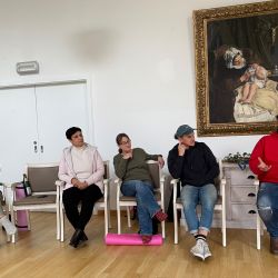 Fünf Personen sitzen in einem Raum vor einem Gemälde und führen ein intensives Gespräch.