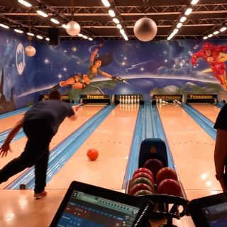 Ein Mann wirft eine Bowlingkugel in einer bunt dekorierten Halle, während eine Frau aufmerksam zuschaut.