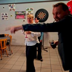 Eine fröhliche Gruppe feiert und spielt Darts in einem gemütlichen Raum mit Bildern an den Wänden.