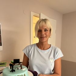 Eine Frau präsentiert stolz eine Torte mit dem Namen "Petra" und detailreicher Schreibtisch-Dekoration.